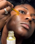 A model applying a dropper of the Scentral Zone 0.5 fl oz Velvet Face Serum with the bottle featured below.