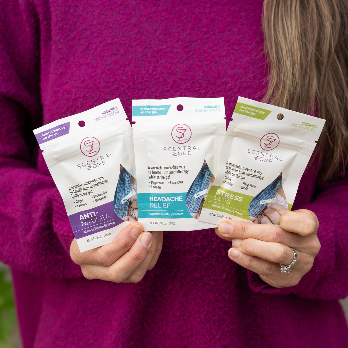 A model holds three Scentral Zone aromatherapy clip-on diffuser pouches including Anti-Nausea, Headache Relief, and Stress Less.