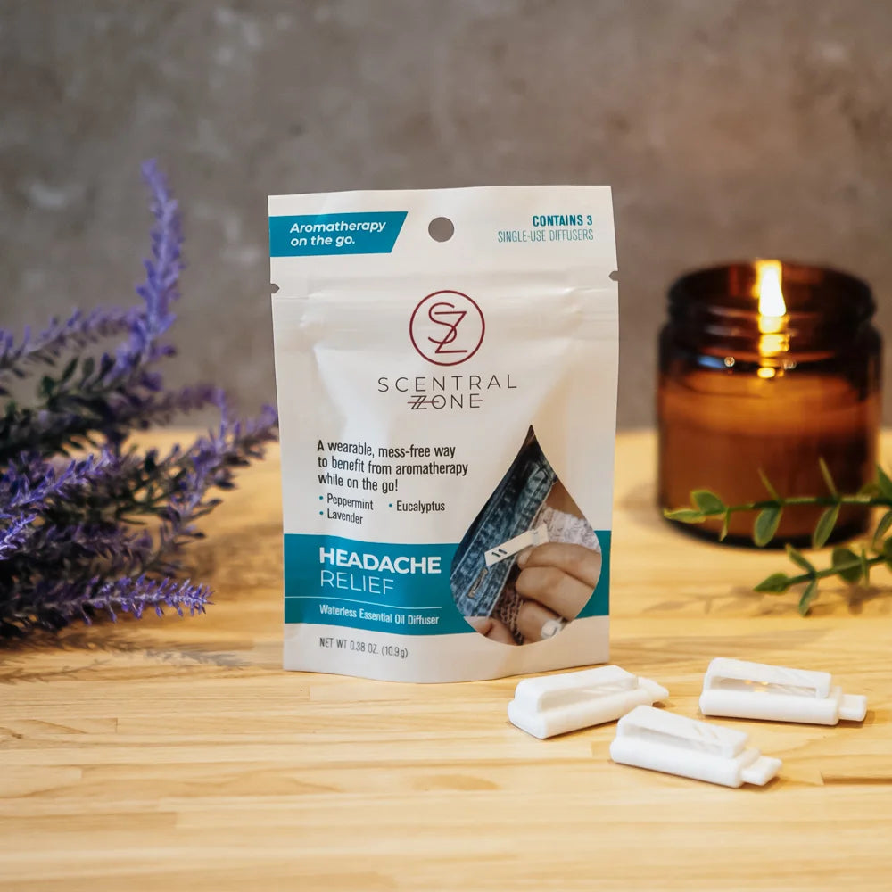 Scentral Zone headache relief clip-on aromatherapy diffuser pouch with a white and teal design on a wooden surface with lavender and a candle in the background highlighting the essential oil ingredients. 