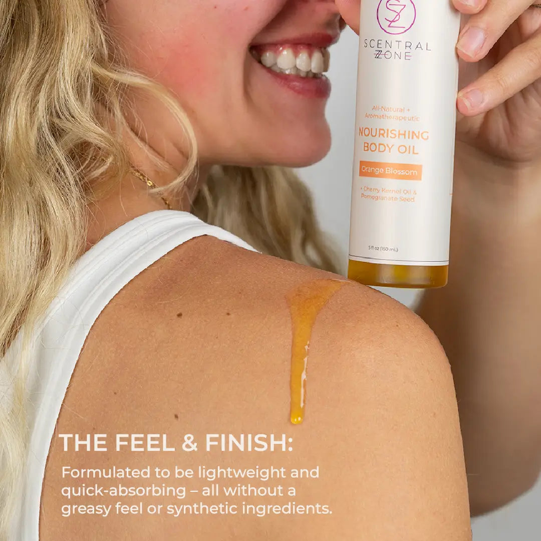 Scentral Zone's 5oz Nourishing Body Oil in Orange Blossom scent in a white bottle is resting on a model's shoulder with oil showing the feel and finish of the body oil that is lightweight and quick absorbing. 