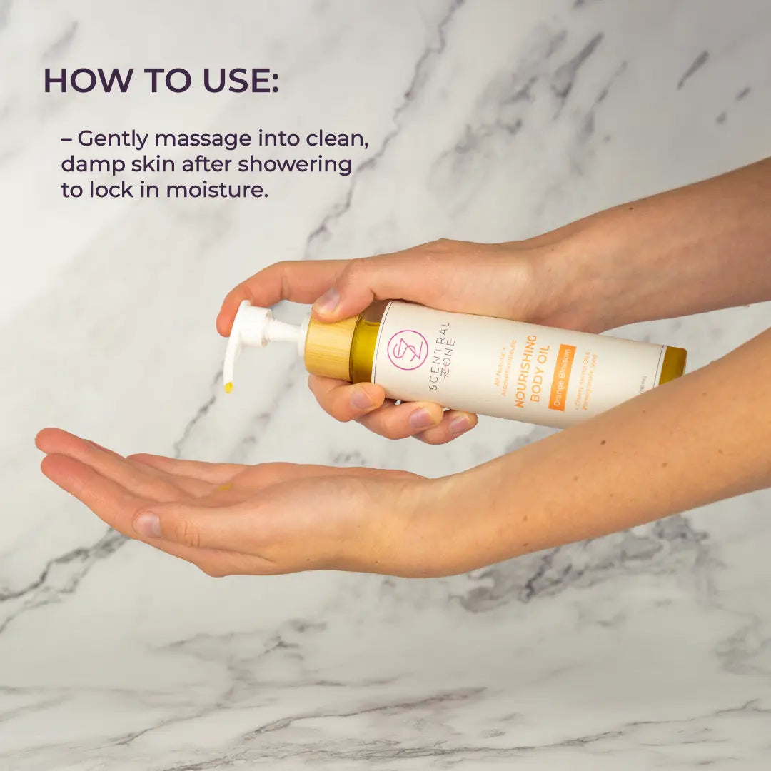 A model pumps Scentral Zone's Nourishing Body oil in Orange Blossom scent onto her hand to show how to use the product. The white bottle is titled to it's side and has a bamboo pump cover. Next to the product is text explaining product directions. 