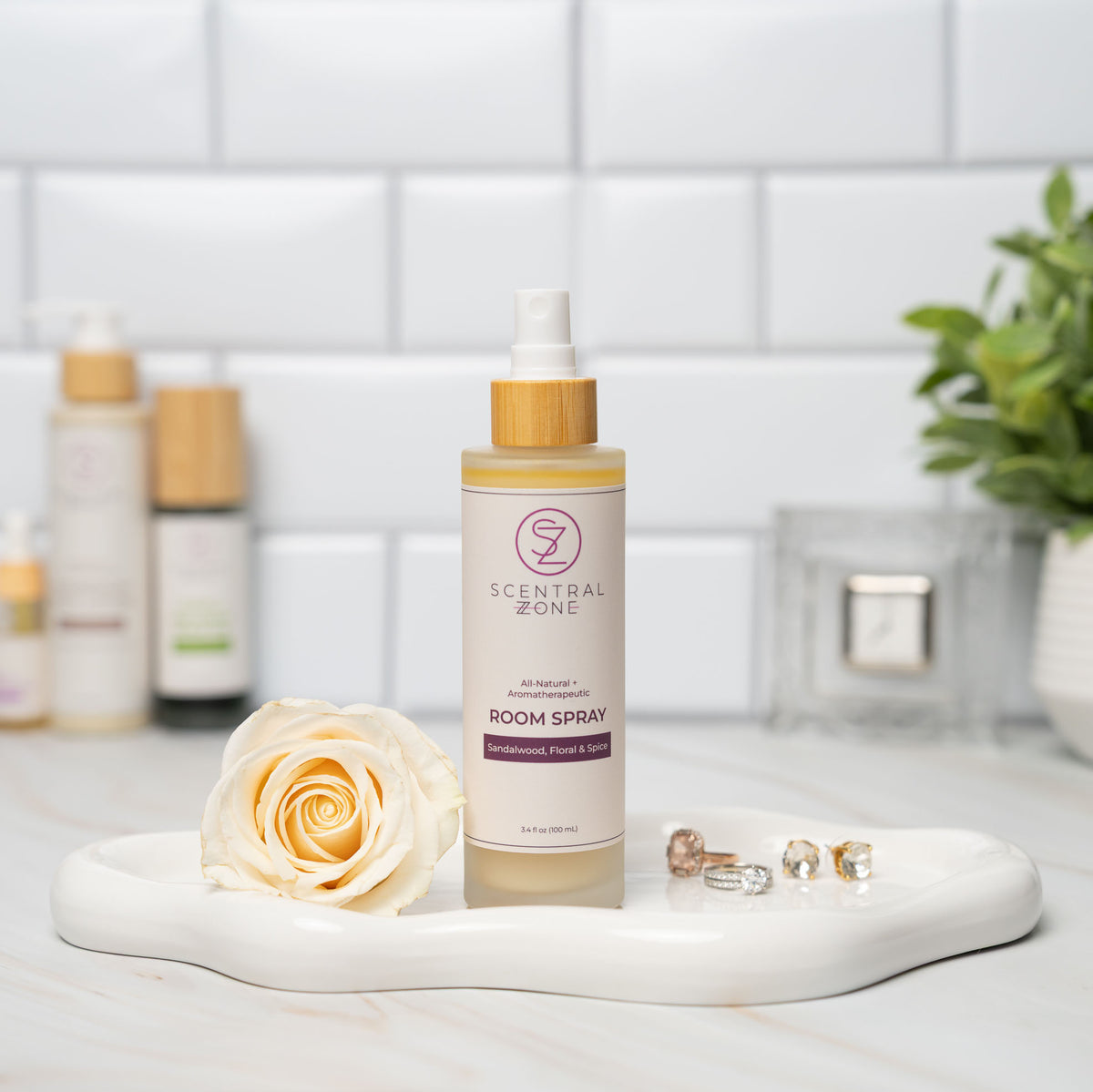 Scentral Zone room spray bottle in scent scandalwood, floral, and spice with a rose and jewelry on a marble tray against a tiled wall.