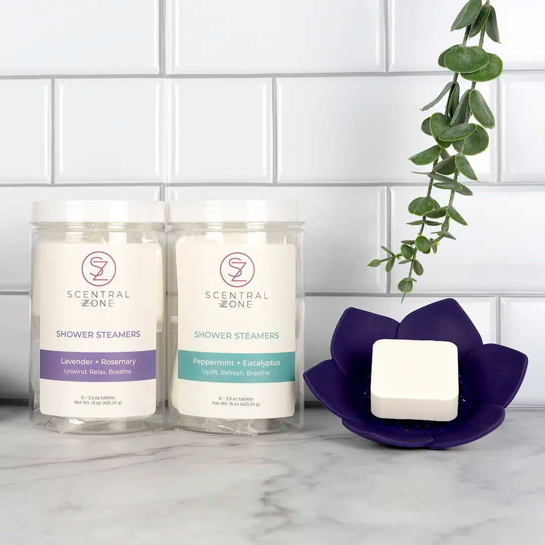 Two Scentral Zone shower steamers containers in jars with a shower steamer in the purple Lotus Dish on a marble surface.