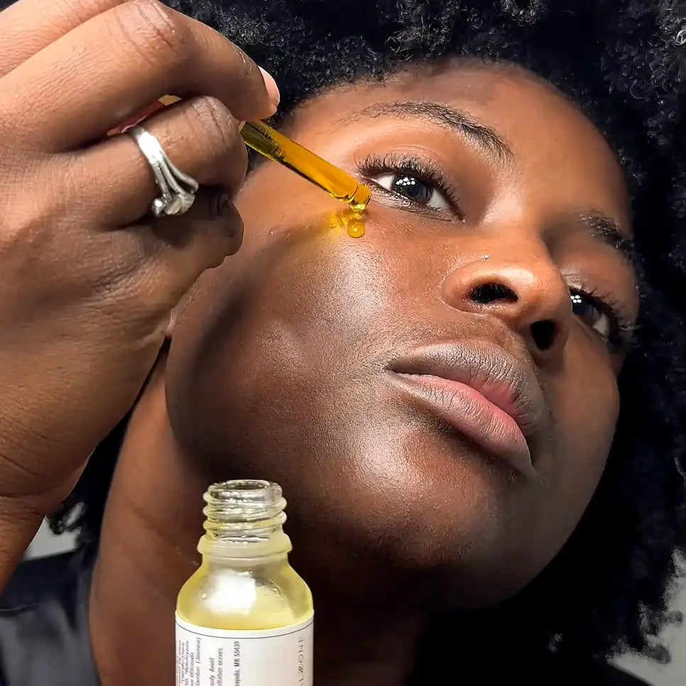 A model applying a dropper of the Scentral Zone 0.5 fl oz Velvet Face Serum with the bottle featured below. 